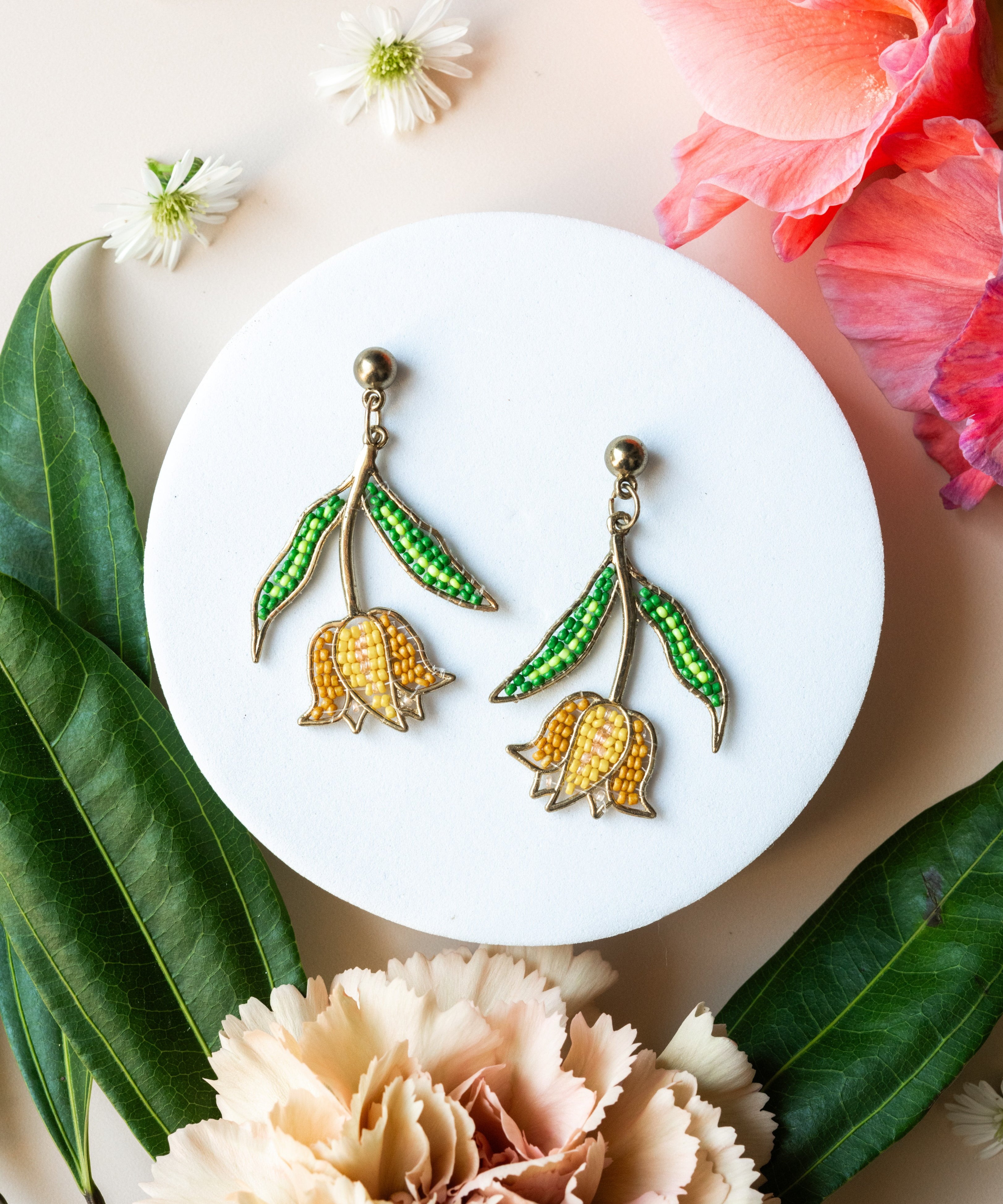 Pair of earrings on a white plate with flowers and leaves around