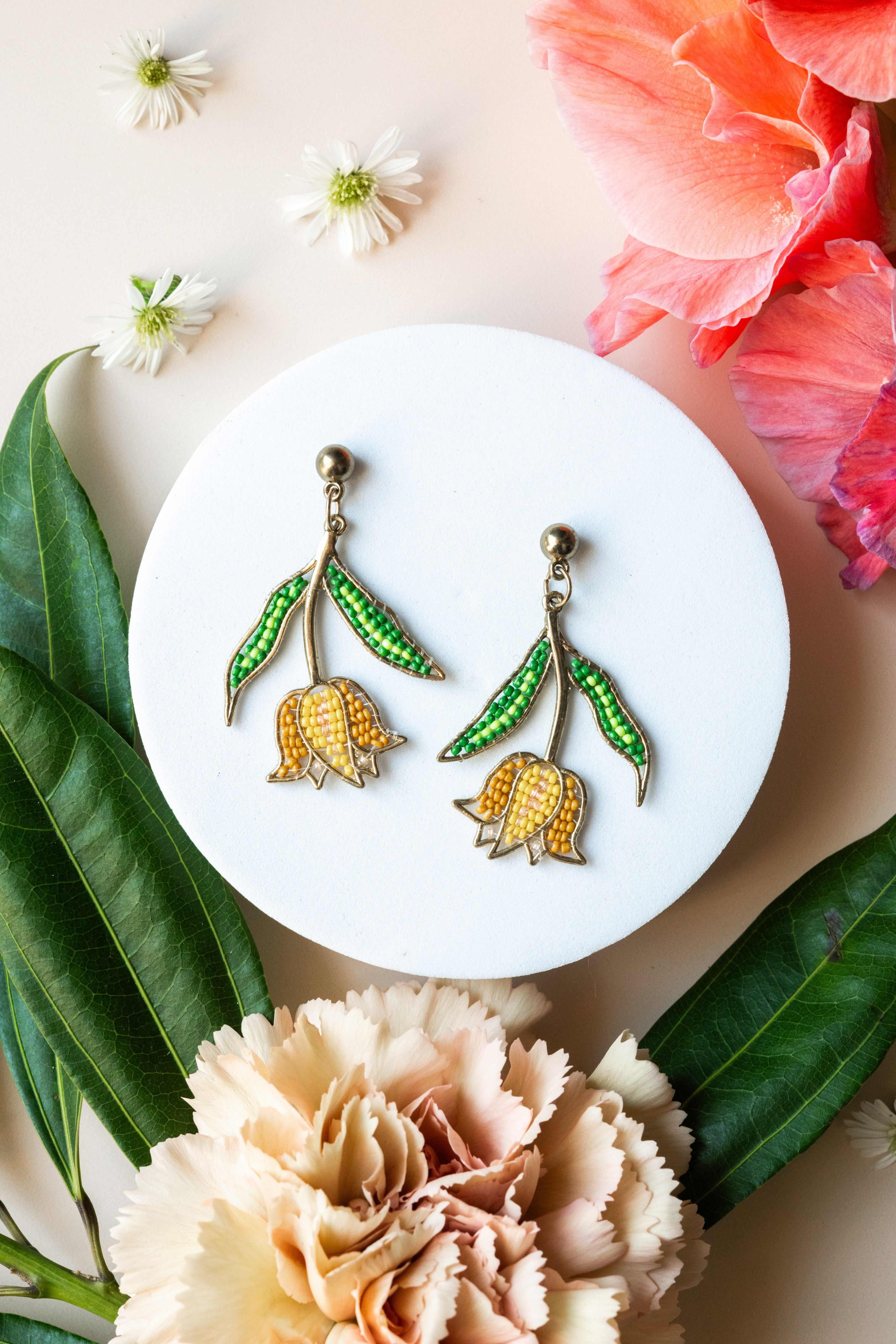 Pair of earrings on a white plate with flowers and leaves around