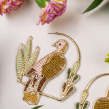 Decorative earrings with bird and plant designs on a light background with flowers and leaves.