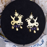 Gold zodiac earrings on a black display pad