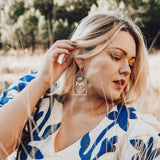 Woman in a white and blue patterned dress standing outdoors with trees in the background