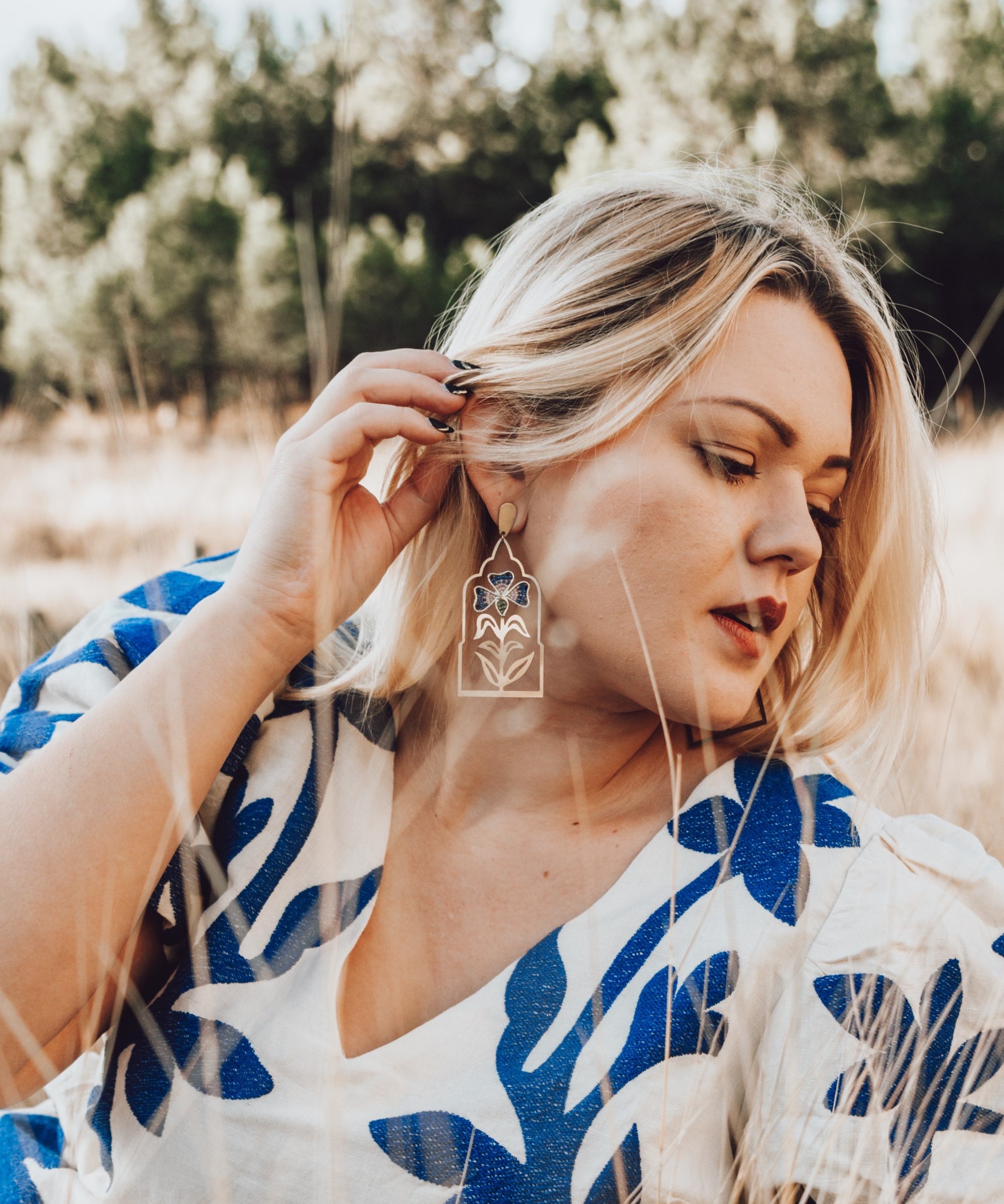 Woman in a white and blue patterned dress standing outdoors with trees in the background