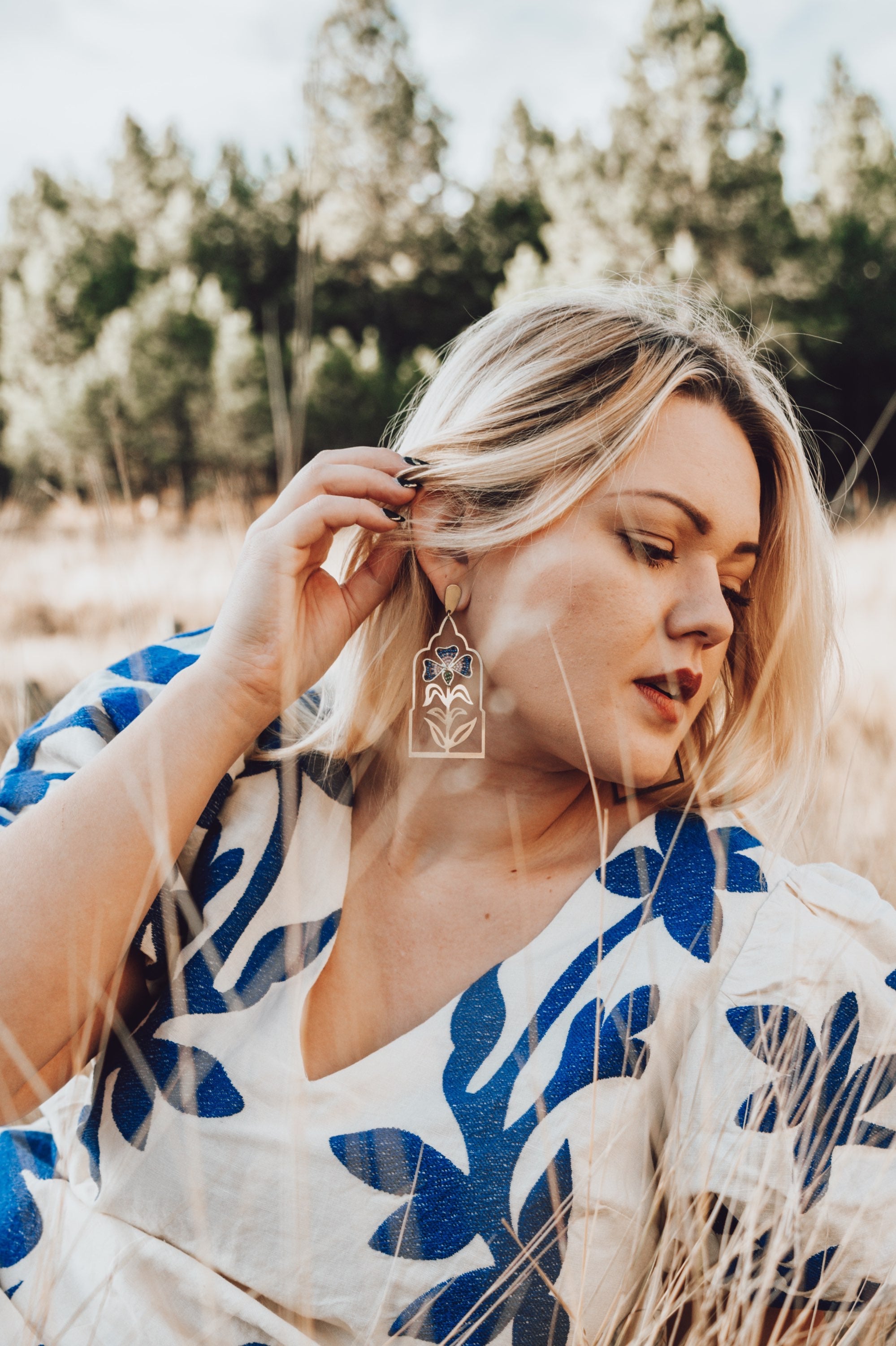 Woman in a white and blue patterned dress standing outdoors with trees in the background
