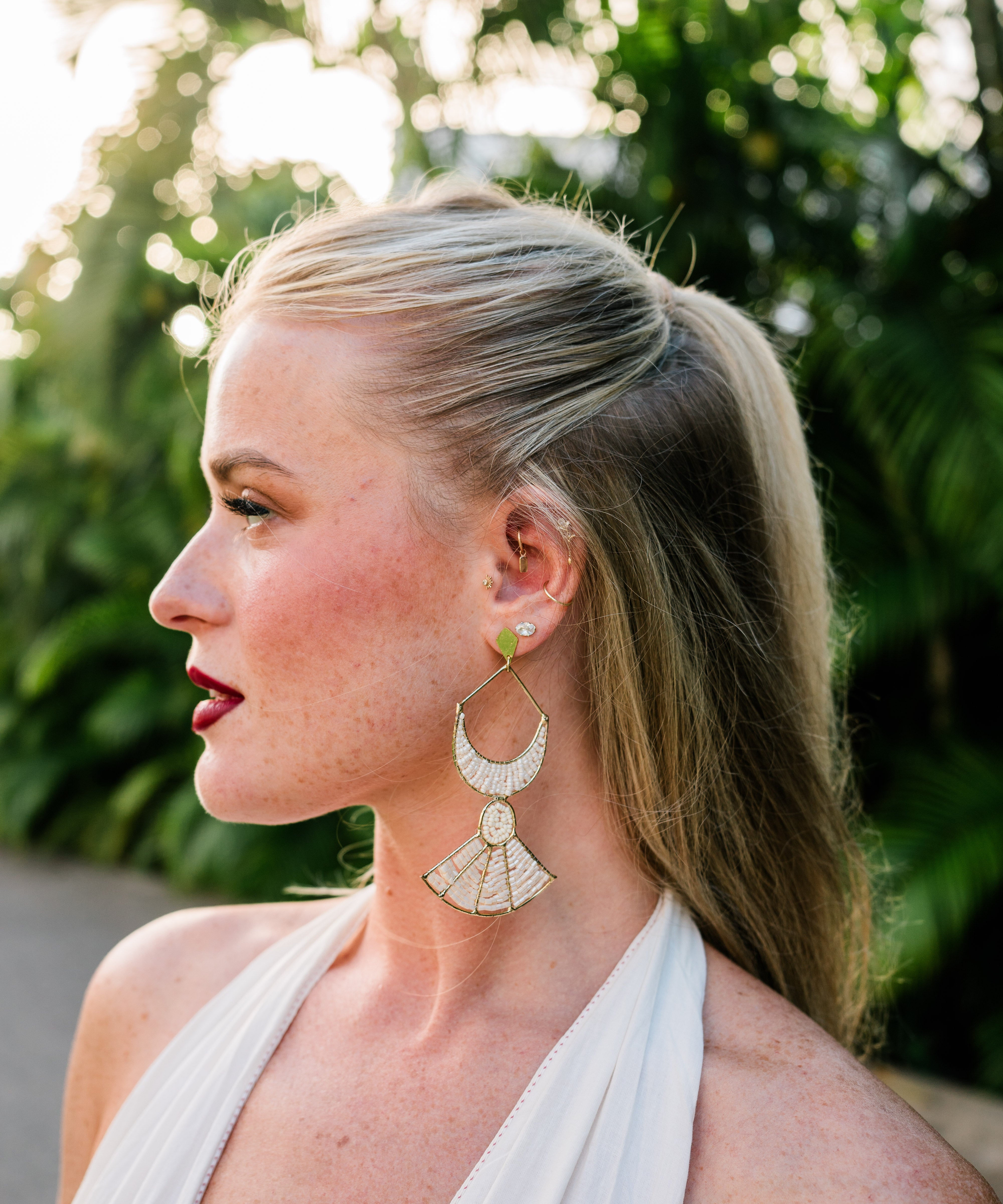 Woman wearing a white dress and earrings with a blurred green background