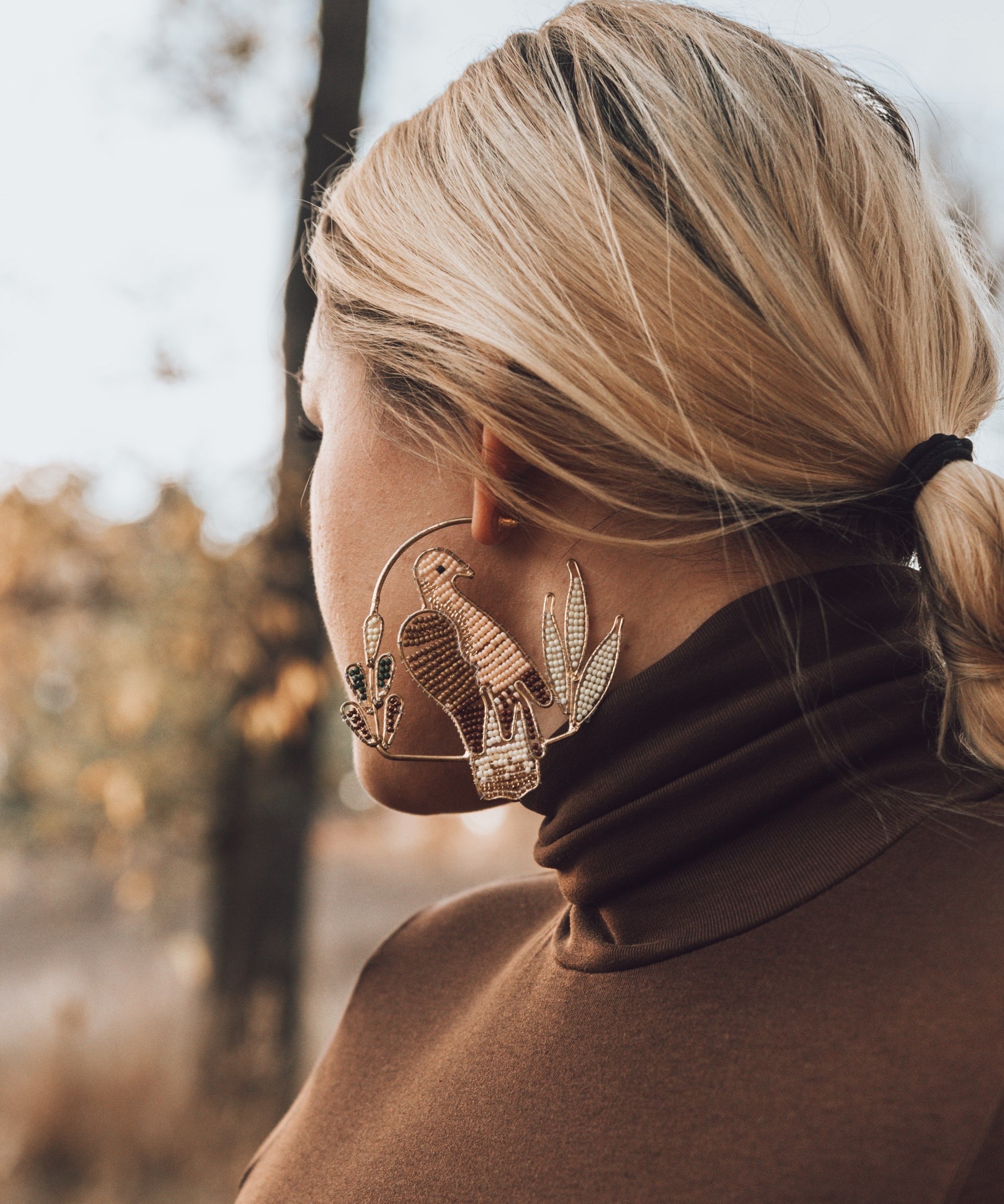 Person wearing large decorative earrings outdoors with a blurred natural background