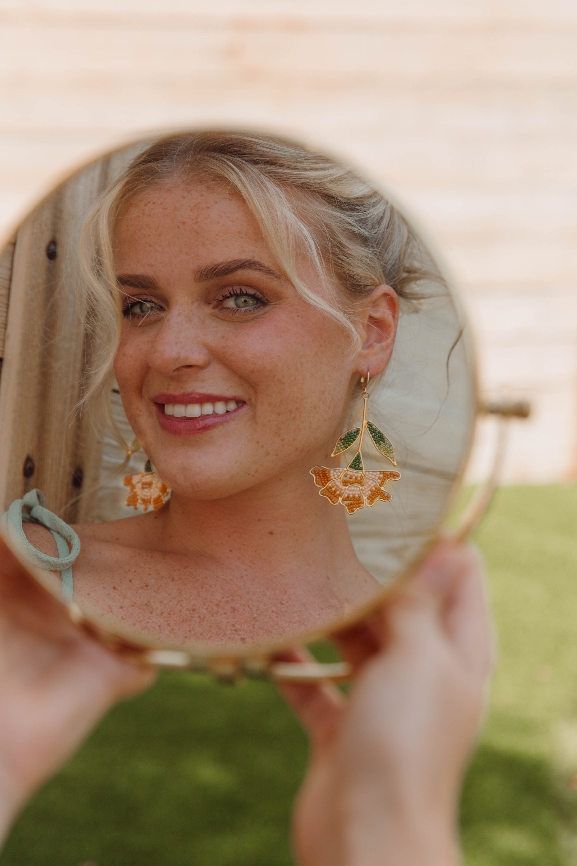 Person holding a round mirror with floral earrings visible