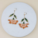 Pair of floral earrings with green leaves on a round stone surface