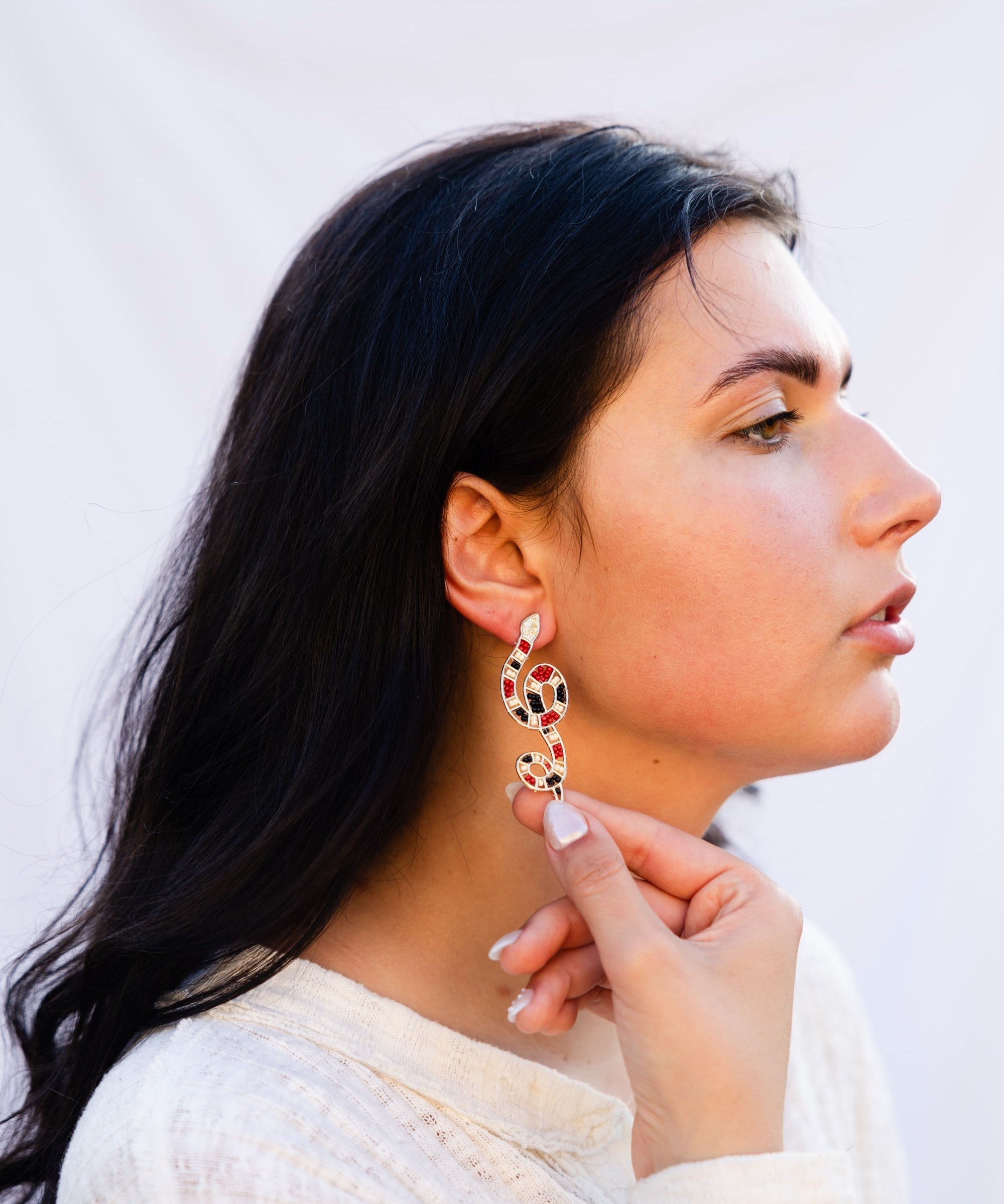 Woman wearing a snake beaded earrings against a plain background