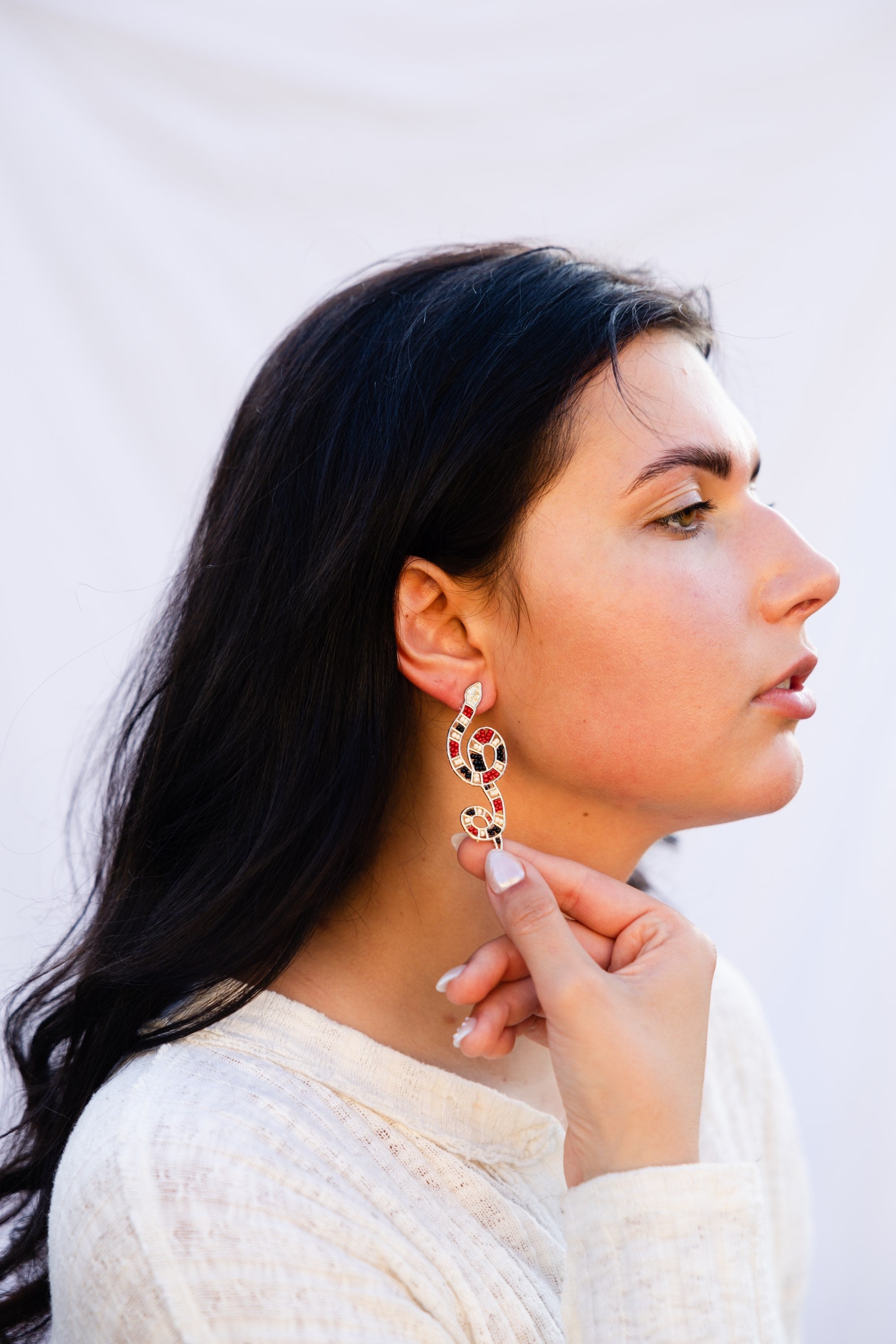 Woman wearing a snake beaded earrings against a plain background