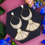 Gold earrings on a black stand with flowers around on a pink background