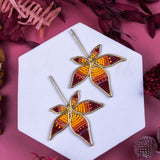 Pair of leaf-shaped earrings on a white hexagonal stand with a pink background