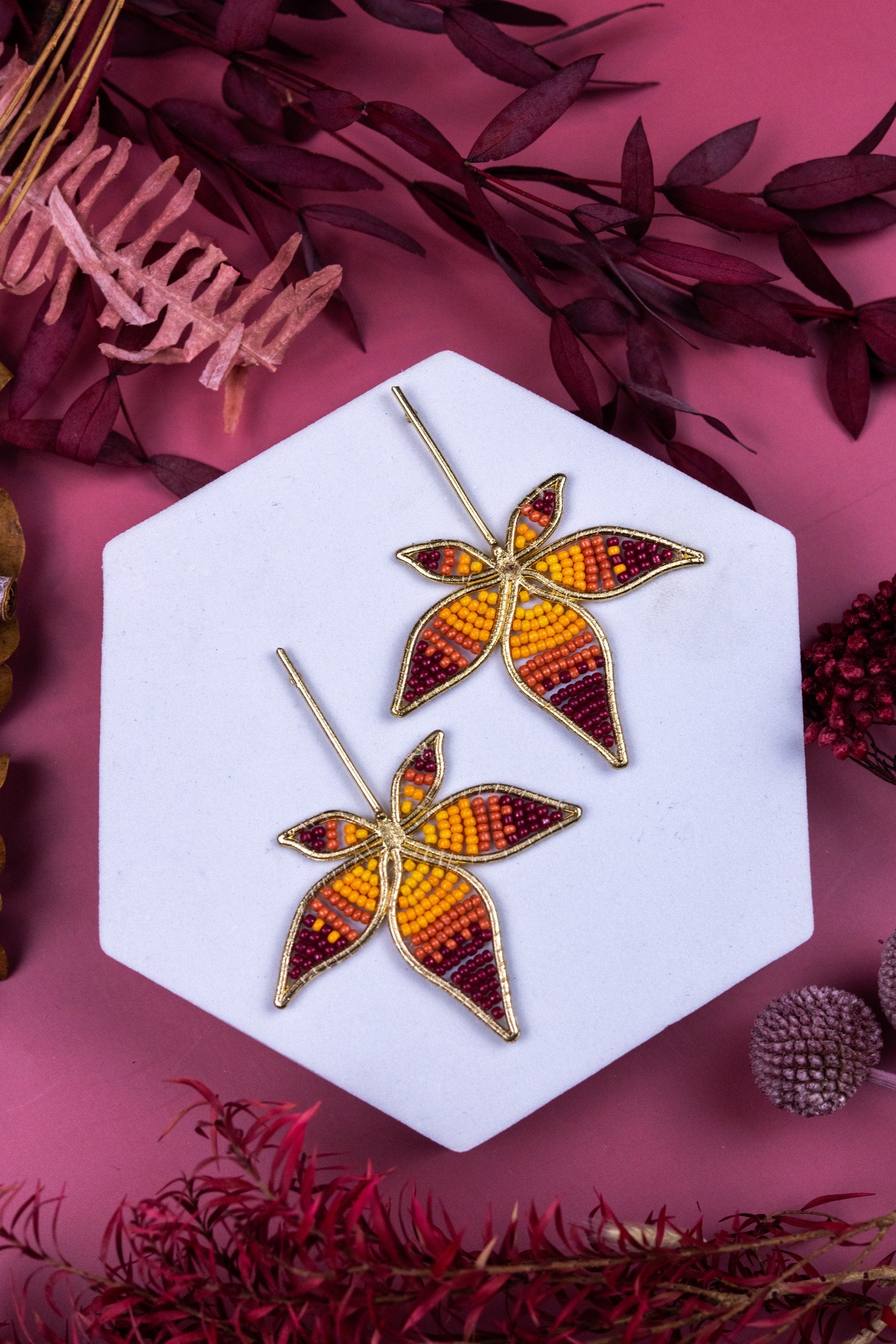 Pair of leaf-shaped earrings on a white hexagonal stand with a pink background