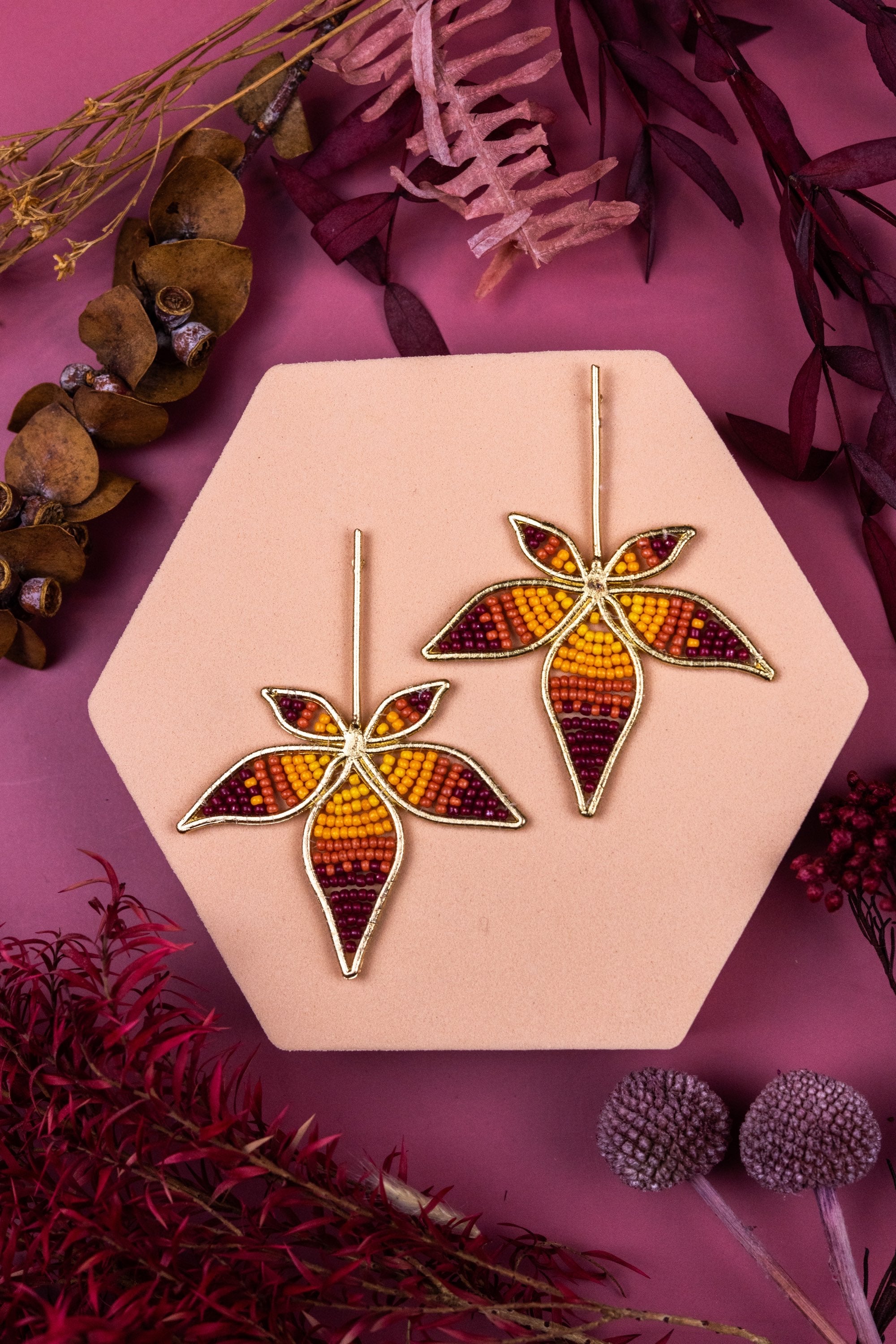 Pair of leaf-shaped earrings on a pink stand with a purple floral background