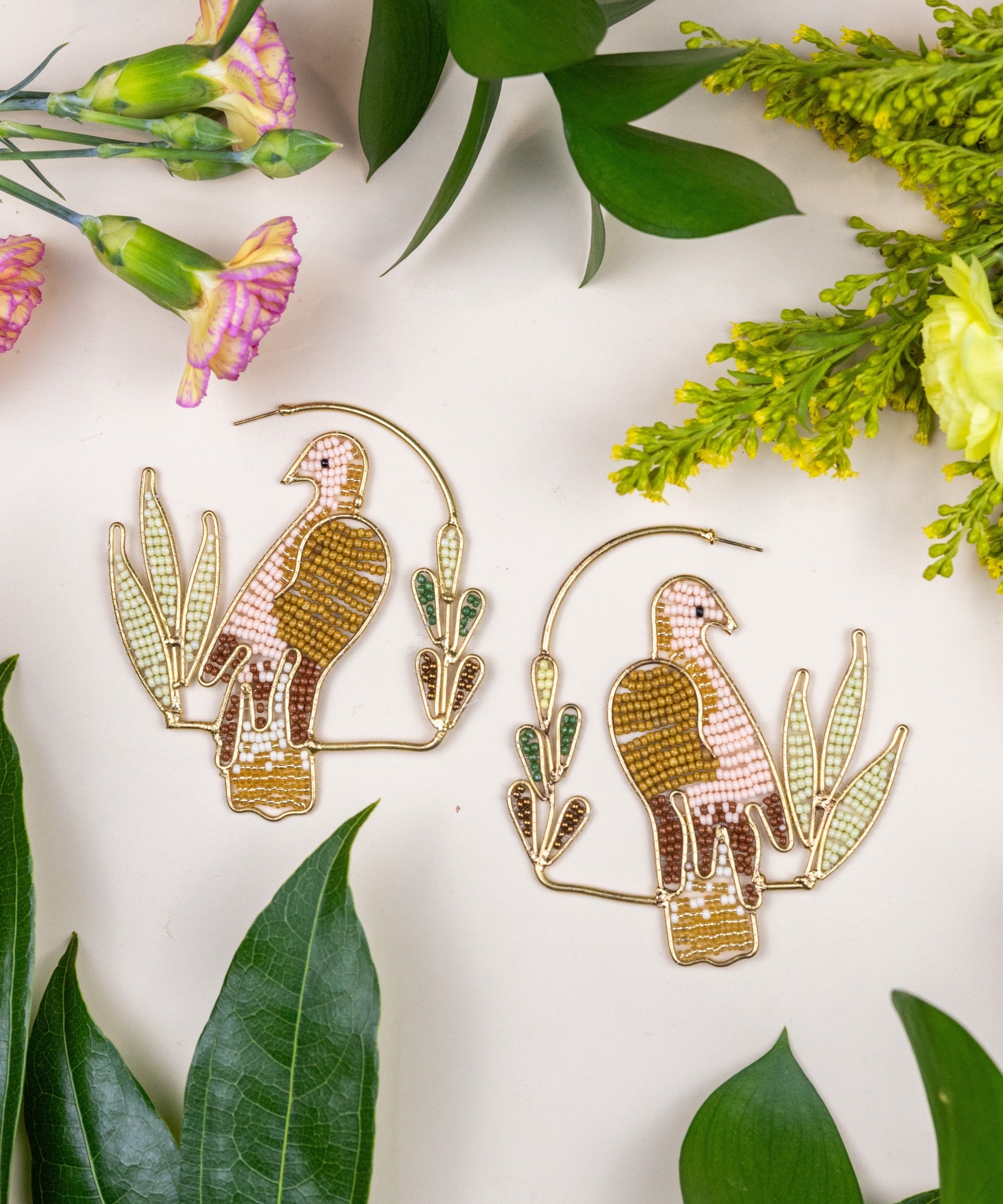 Birds of Morning Hoop - Gold parrot earrings on a white background with green leaves and flowers.