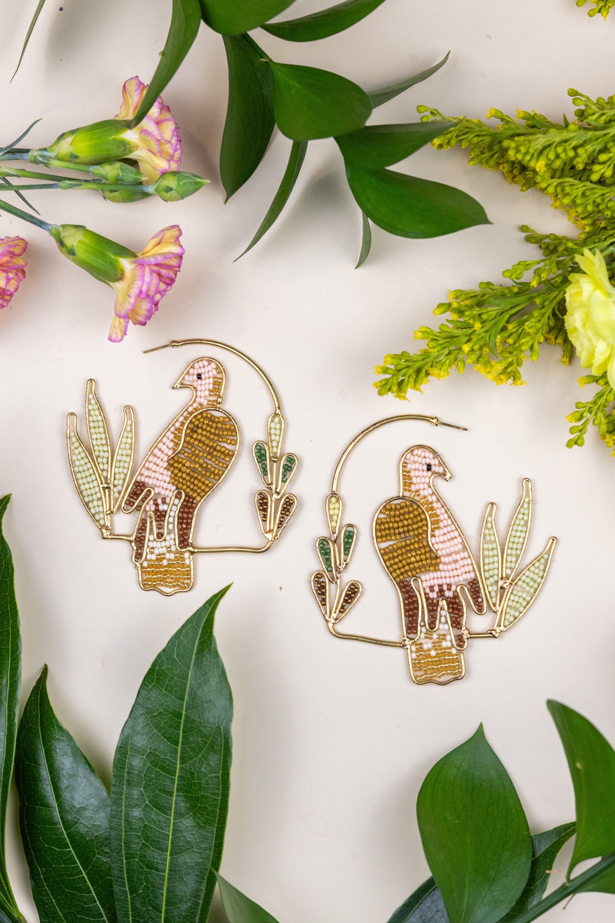 Birds of Morning Hoop - Gold parrot earrings on a white background with green leaves and flowers.