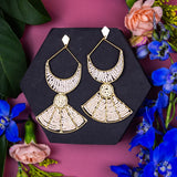 Gold earrings on a black stand with flowers on a pink background