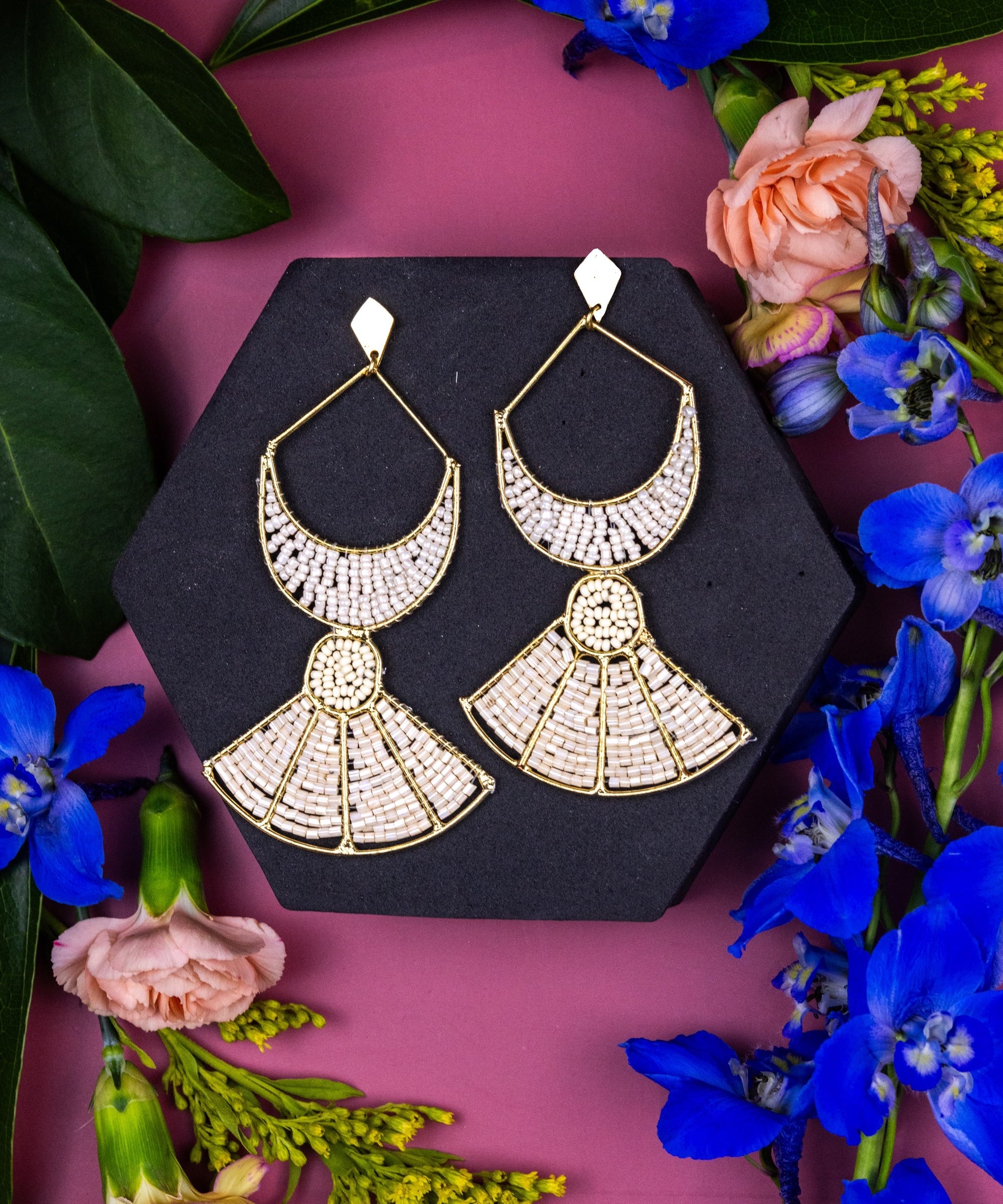 Gold earrings on a black stand with flowers on a pink background
