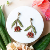 Pair of floral earrings on a white dish with flowers and leaves around